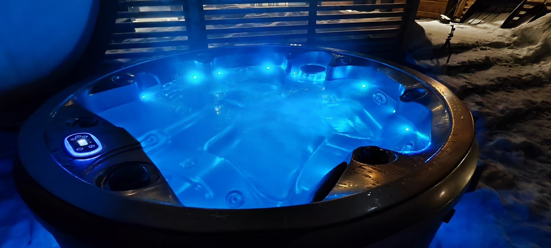 Ein beleuchteter Whirlpool mit blauem Wasser dampft in einer verschneiten Winternacht in Kuusamo, Finnland, und lädt zum Entspannen ein.