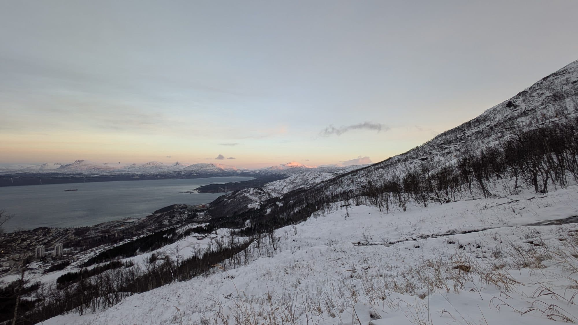 Weiter Panoramablick von einem Berg oberhalb Narviks auf den Fjord, die Stadt und schneebedeckte Gipfel.
