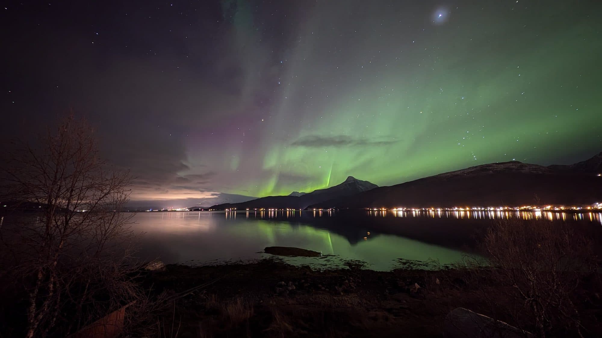 Weites grün-violettes Polarlicht spiegelt sich im ruhigen Fjordwasser bei Ballangen.