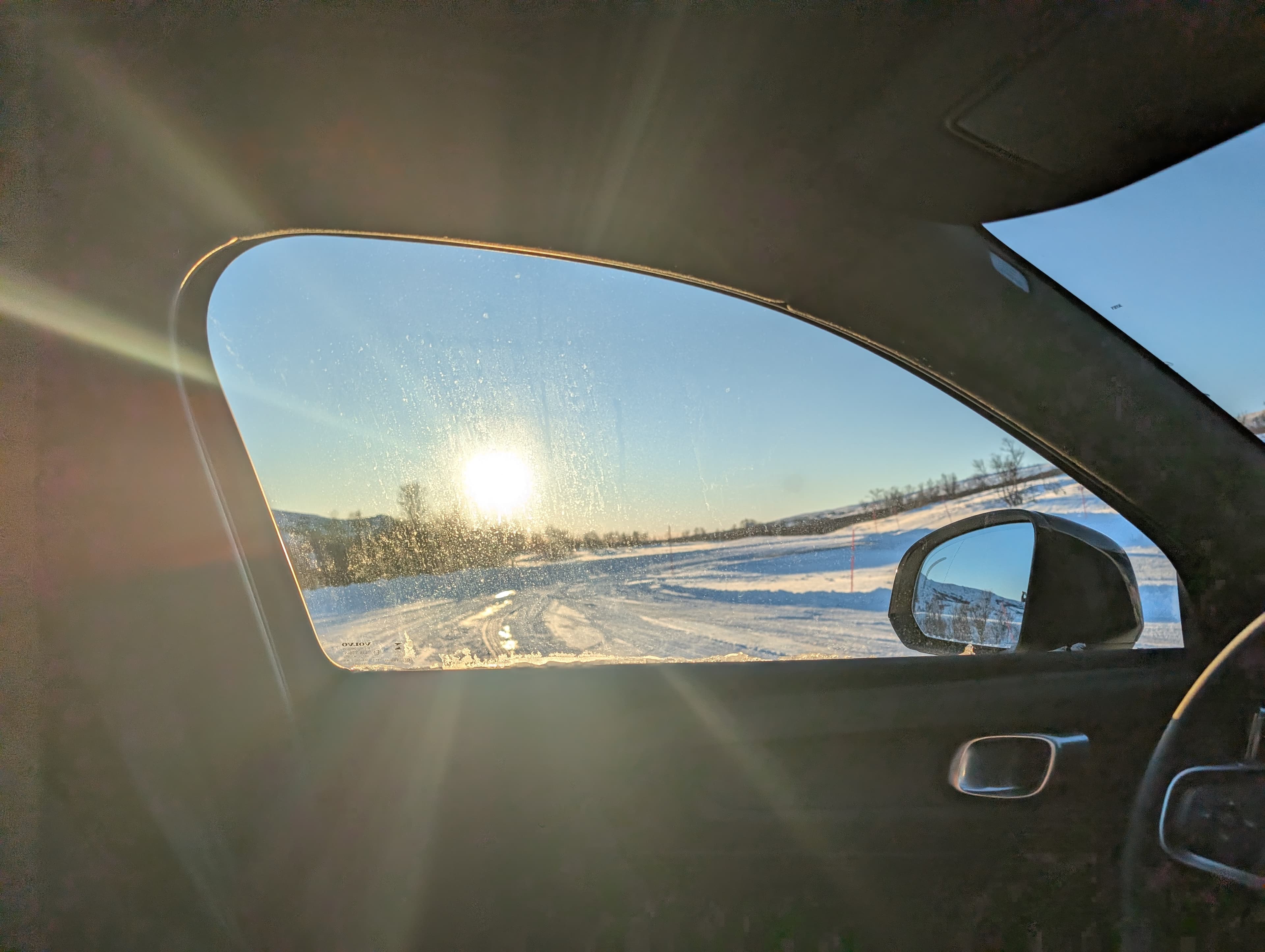 Eine Aussicht aus dem Autofenster auf eine schneebedeckte Straße bei tiefstehender Wintersonne in Nordnorwegen. Die Szene vermittelt das Gefühl einer einsamen Winterreise durch die karge Landschaft.