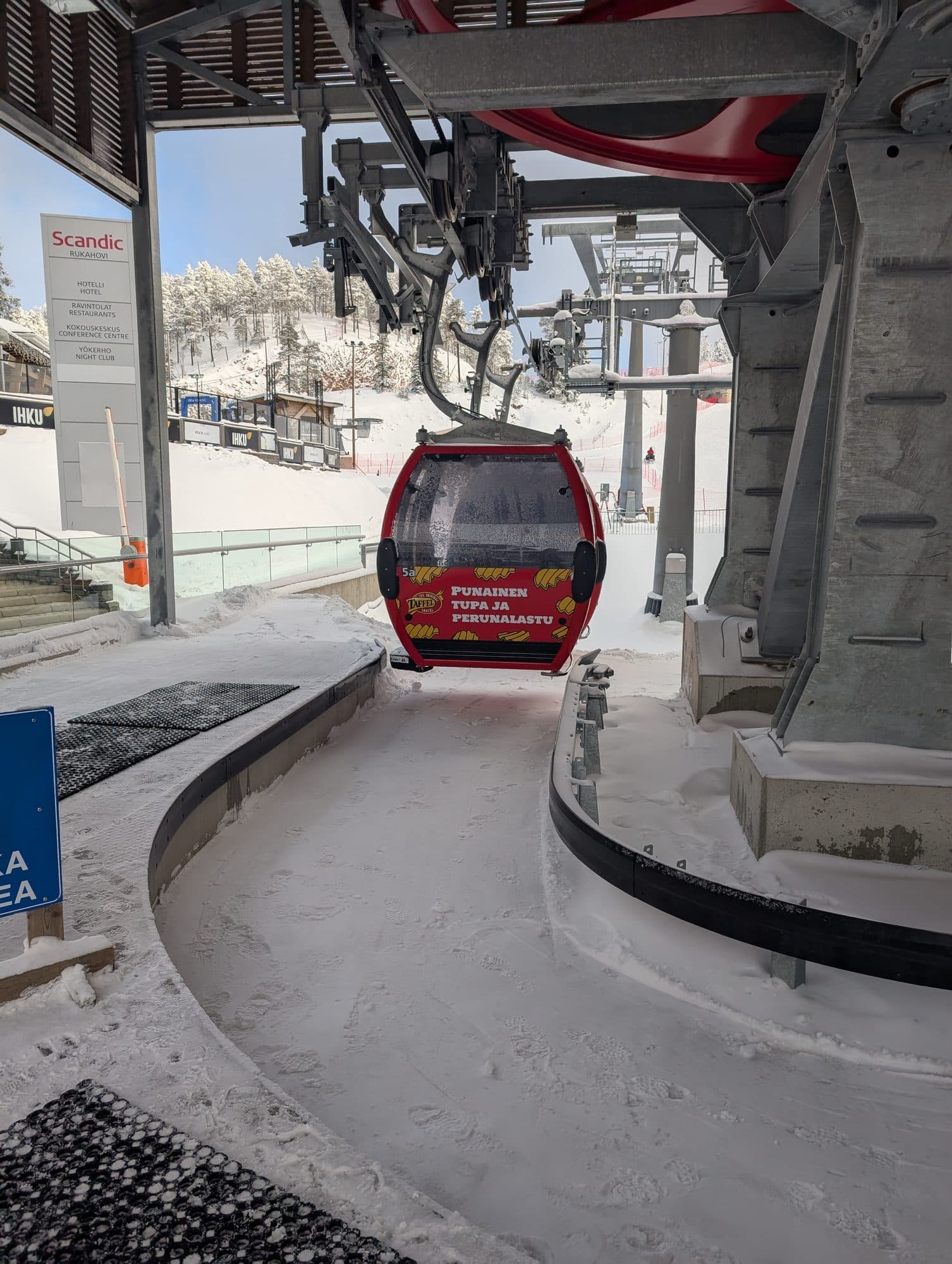 Eine rote Gondel der Seilbahn am Rukatunturi schwebt in die Bergstation ein, im Hintergrund ist das Scandic Rukahovi zu erkennen.