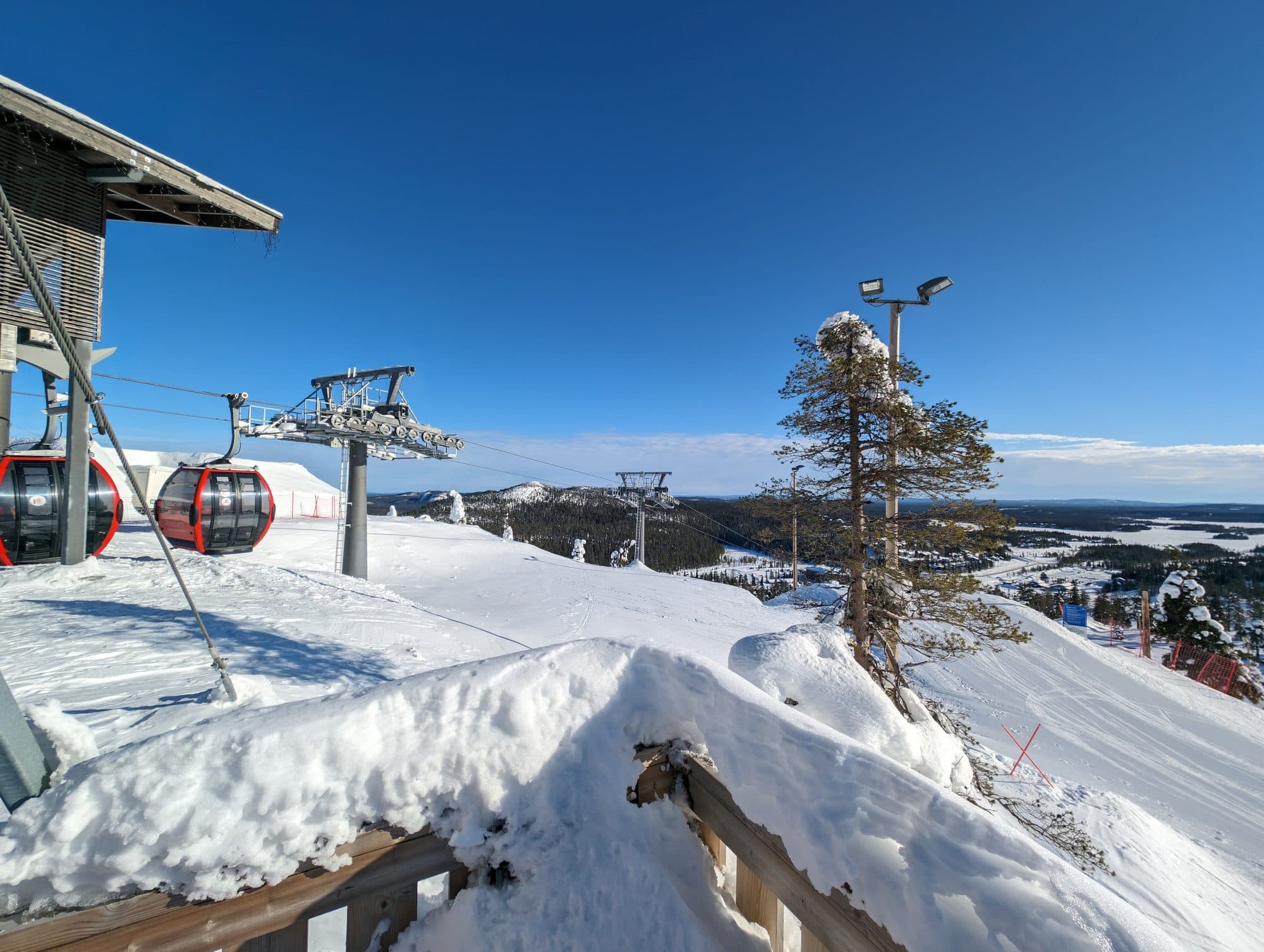 Bergstation der Gondelbahn in Ruka mit auffälligen roten Kabinen vor blauem Himmel, im Hintergrund die verschneite Fjell-Landschaft von Kuusamo.