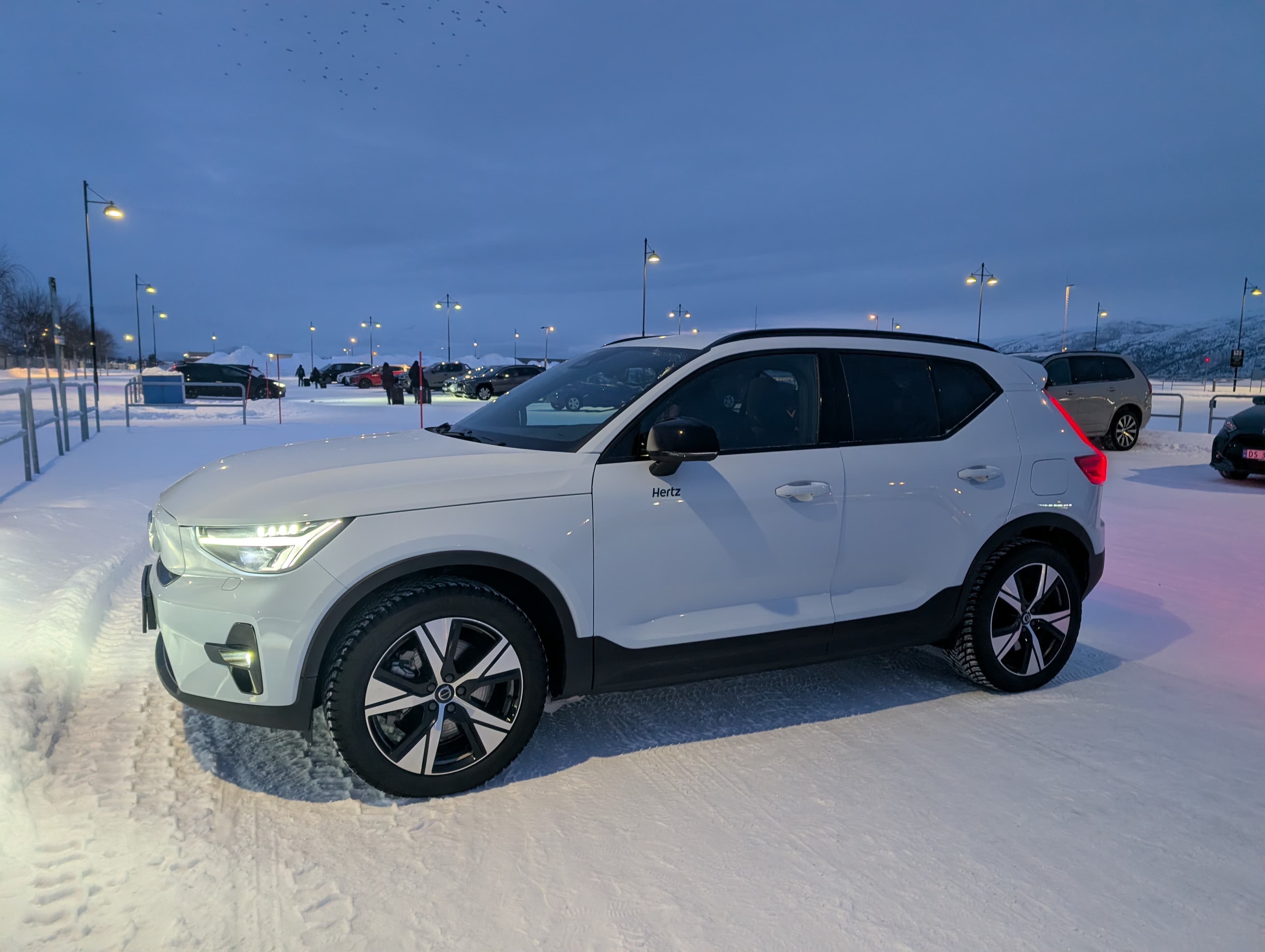 Grünes Polarlicht über einer verschneiten Hügellandschaft in Nordnorwegen mit einem kleinen beleuchteten Haus.