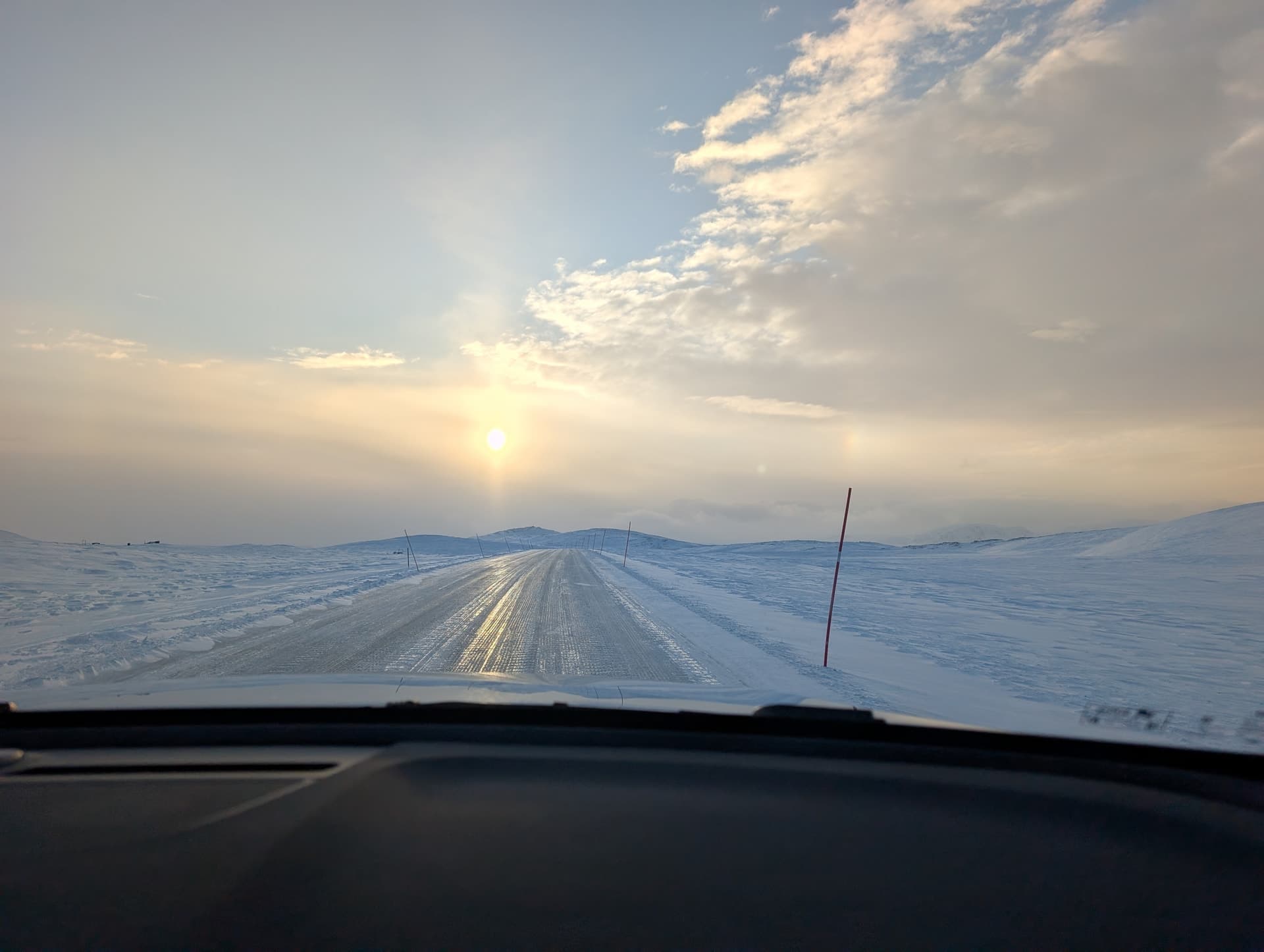 Eine Autofahrt durch eine weite, verschneete arktische Landschaft bei tiefstehender Sonne. Die Szene vermittelt das Gefühl von Freiheit und Kälte im hohen Norden.