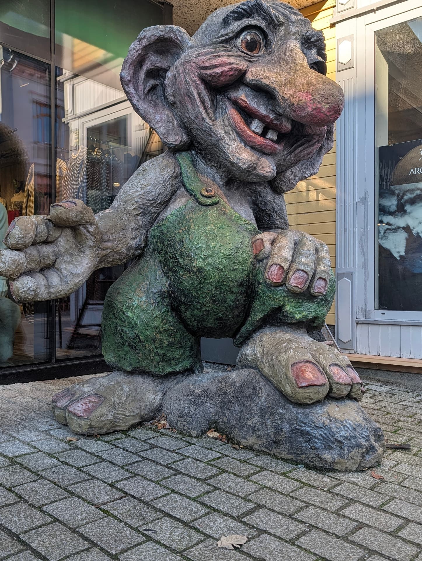 Eine große, farbige Troll-Skulptur steht auf einem gepflasterten Gehweg vor einem Geschäft in Nordnorwegen.