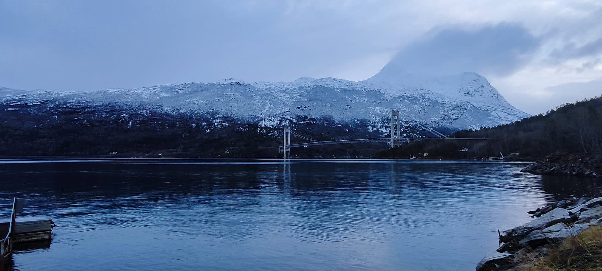 Die Hålogalandsbrücke bei Narvik überspannt den Fjord vor schneebedeckten, wolkenverhangenen Bergen.