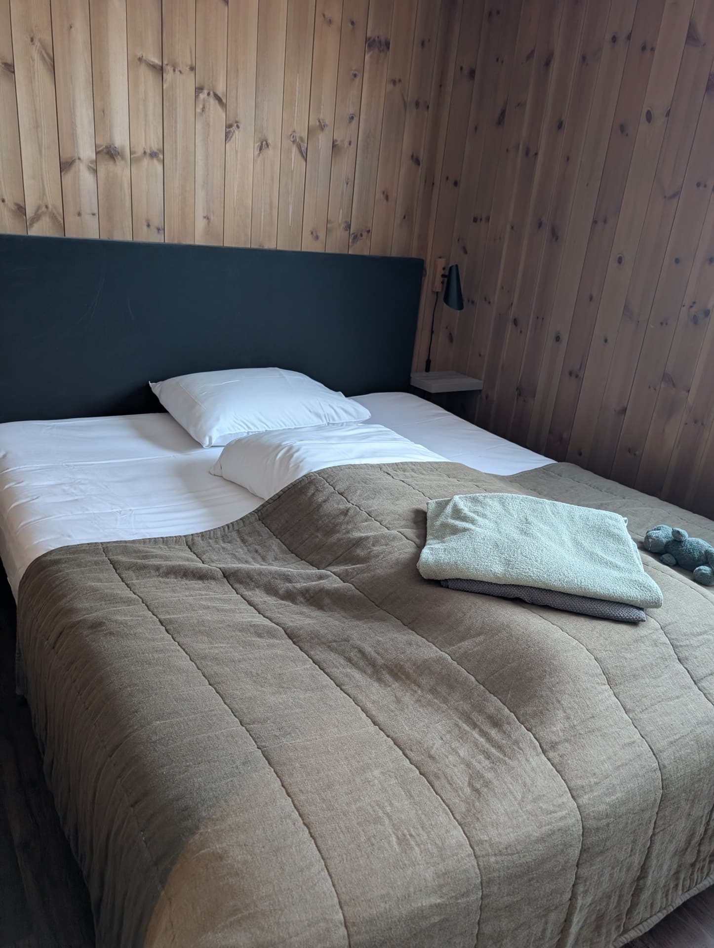 Ein sauber gemachtes Doppelbett in einem rustikalen Holzhaus, das eine gemütliche Atmosphäre für die Erholung nach einer Nordnorwegen-Reise vermittelt.