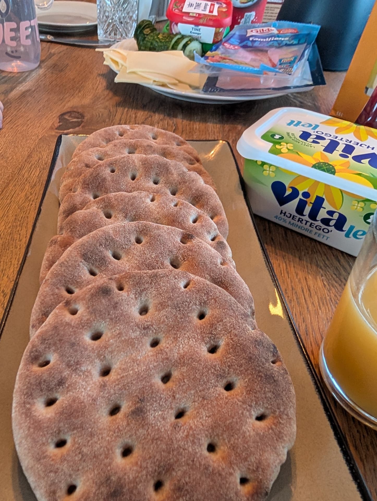 Eine Nahaufnahme von knusprigen norwegischen Vollkornbiskuitbroten auf einem Teller, begleitet von Margarine und weiteren Frühstückszutaten. Die Szene vermittelt eine authentische, gemütliche skandinavische Atmosphäre.