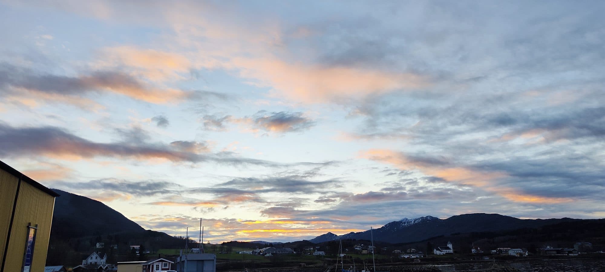 Dramatischer Sonnenuntergang über dem Fischerdorf Ballangen mit orange-rosa gefärbten Wolken.