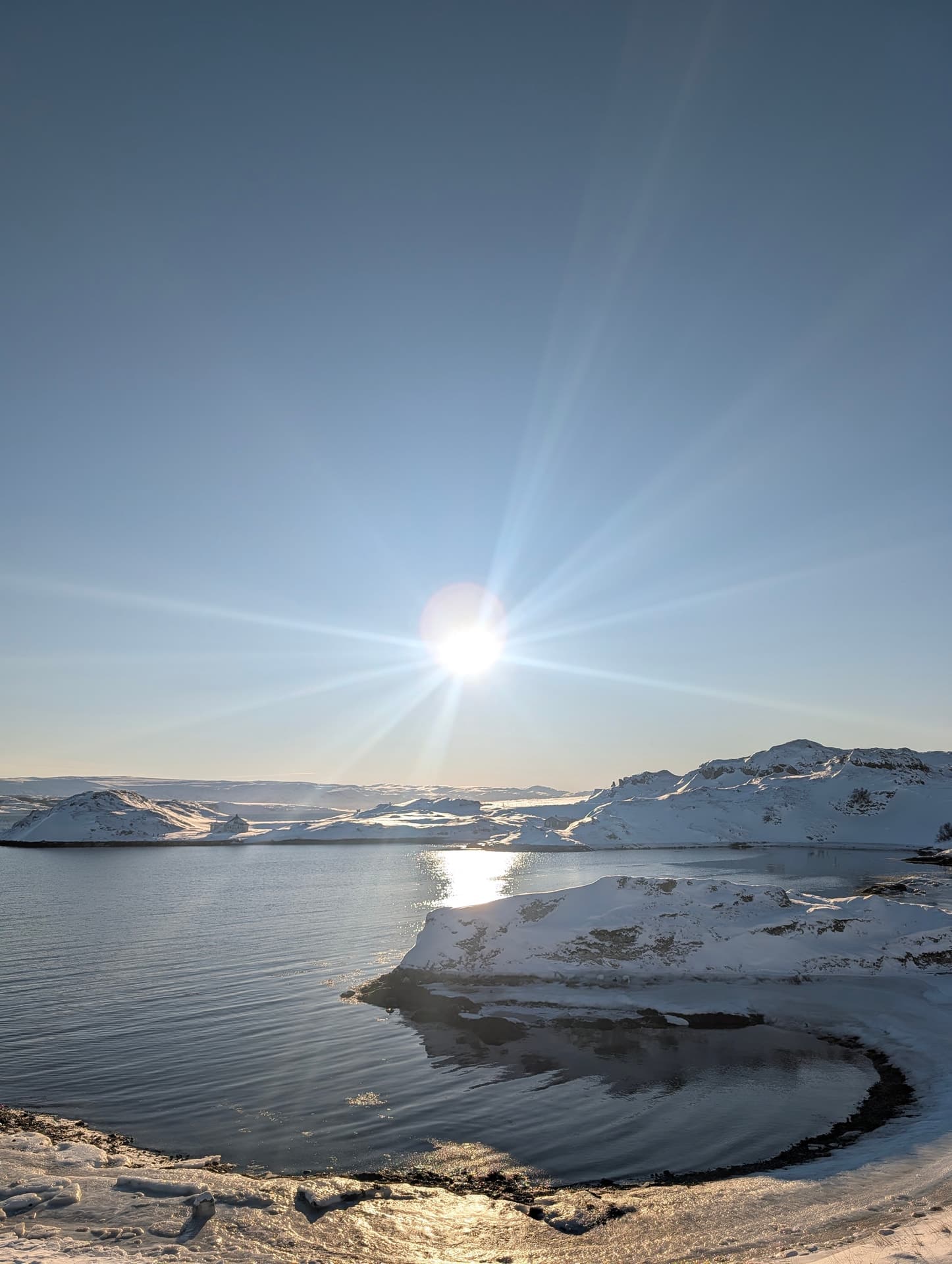 Eine winterliche Küstenlandschaft in Nordnorwegen mit tiefstehender Sonne, die einen Sterneneffekt erzeugt und auf dem ruhigen Wasser reflektiert wird.