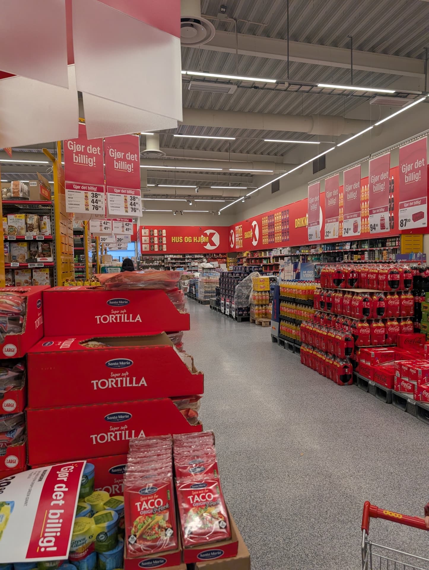 Blick in einen norwegischen Supermarkt mit roten Aktionsplakaten und gefüllten Regalen. Die Szene wirkt alltäglich und funktional, typisch für eine Einkaufsrunde während einer Reise.